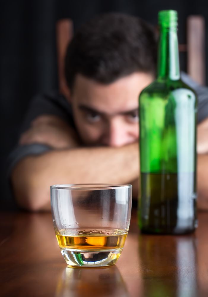 Glass of whisky with an out of focus drunk and depressed man in the background